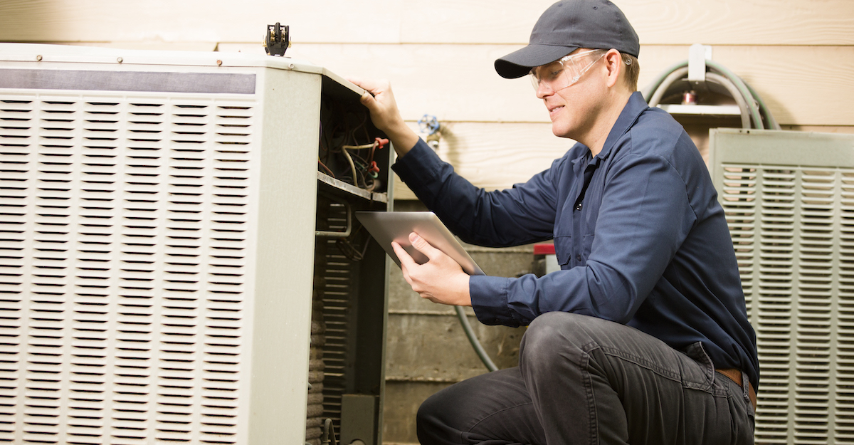 Field service hvac employee works on home unit while holding a tablet